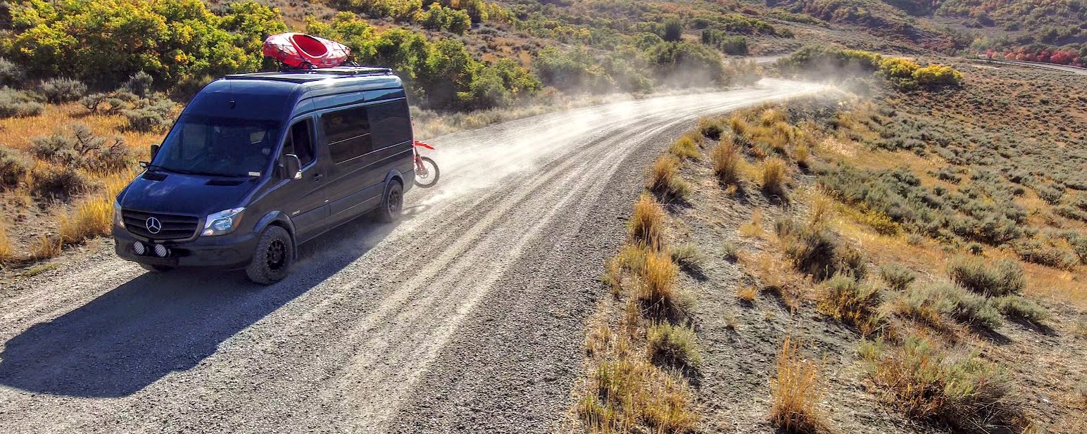 Our finished Mercedes Sprinter adventure van exploring a scenic mountain dirt road with a kayak and dirt bike